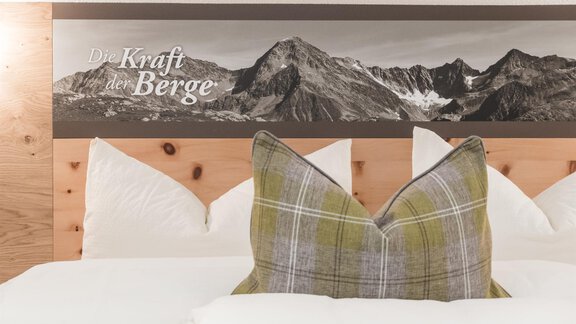 A modern bedroom with a cozy pillow and wall paneling that features impressive mountains. The inscription "The Power of the Mountains" highlights the alpine atmosphere. - Garni Ötztal ROOMS & APARTS - Zwieselstein