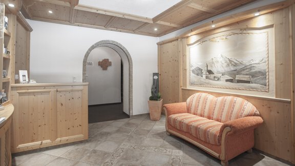An inviting reception area with wooden furniture and a comfortable sofa. A large picture of a mountain landscape hangs on the wall. - Garni Ötztal ROOMS & APARTS - Zwieselstein