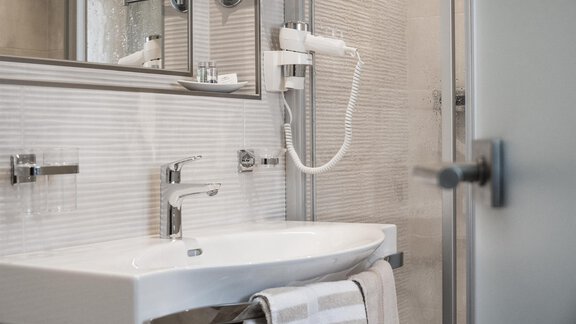 A modern bathroom with a sink and a large mirror. The walls are painted in neutral tones. - Garni Ötztal ROOMS & APARTS - Zwieselstein