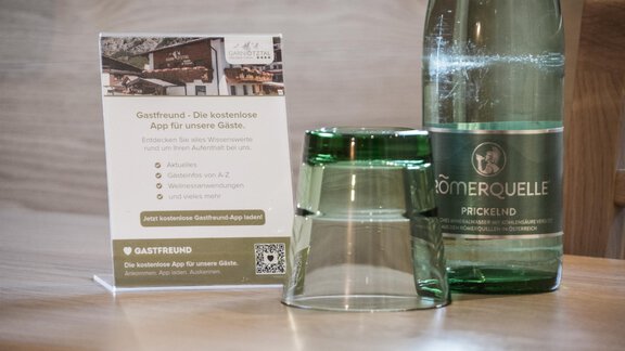 A stylish table with a bottle of water and a glass. Next to the glass is an information card about an app for guests. - Garni Ötztal ROOMS & APARTS - Zwieselstein
