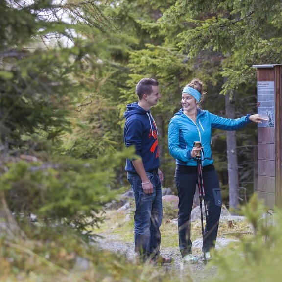 A couple is hiking in the forest and looking at an information sign. The surroundings are green and close to nature, ideal for outdoor activities. - ÖTZTAL TOURISMUS - Information Längenfeld - Längenfeld