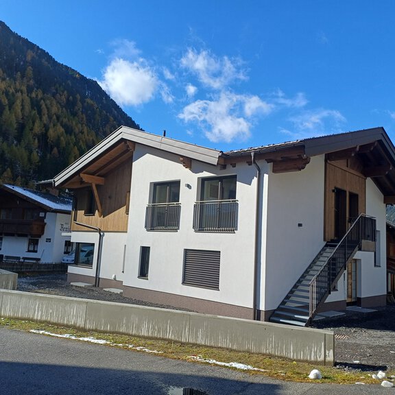 A modern house in the mountains with a bright facade and a balcony. In the background, trees and mountains are visible. - Apart Monte Vista - Gries