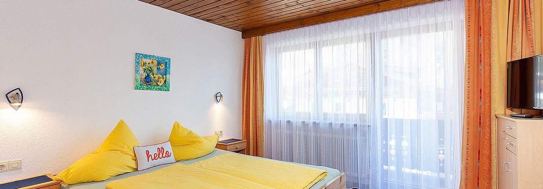A cozy bedroom with a large bed and colorful pillows. The windows are bright and provide plenty of daylight. - Berghof Schöpf - Gries