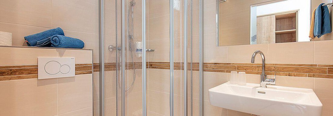 A modern bathroom with a shower and a sink. The walls are light-tiled and there are blue towels ready. - Berghof Schöpf - Gries