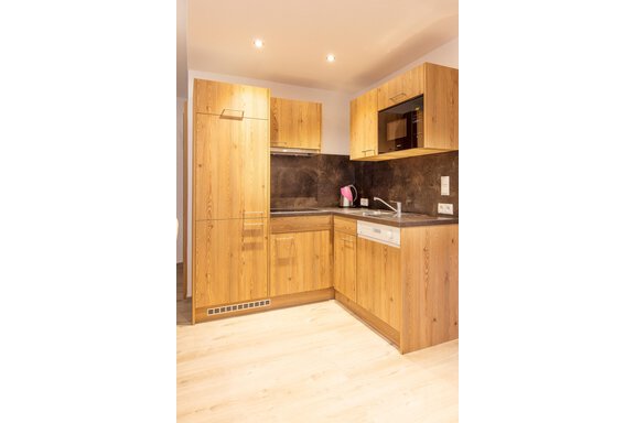 A modern kitchen with wood cabinets and a black countertop. It features a dishwasher and a microwave. - Berghof Schöpf - Gries