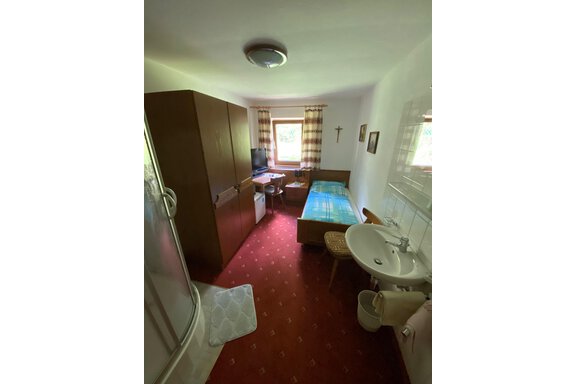 WhatsApp Image 2026-05-28 at 10.02.02 (3) Ein einfaches Zimmer mit einem Bett, einem Schreibtisch und einem Fernseher. In der Ecke befindet sich eine Dusche und ein Waschbecken. - Haus Bergkristall - Gries