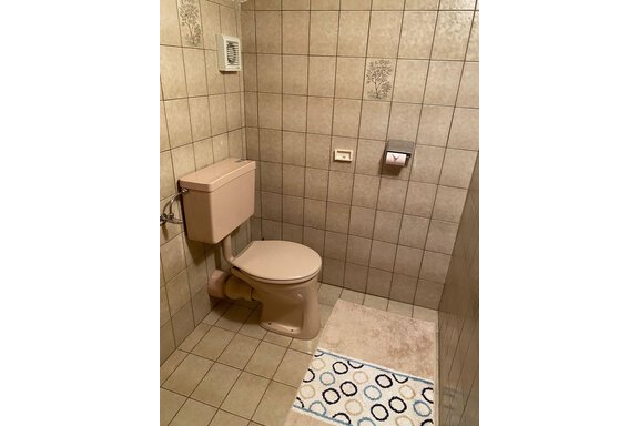 Ein einfaches Badezimmer mit einer hellbeigen Toilette und gefliesten Wänden. Der Boden ist mit einem bunten Teppich dekoriert. - Haus Bergkristall - Gries