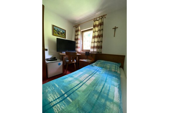 Ein einfaches Schlafzimmer mit einem Bett, einem Fernseher und einem kleinen Kühlschrank. Das Fenster bietet Tageslicht und der Raum hat eine gemütliche Atmosphäre. - Haus Bergkristall - Gries