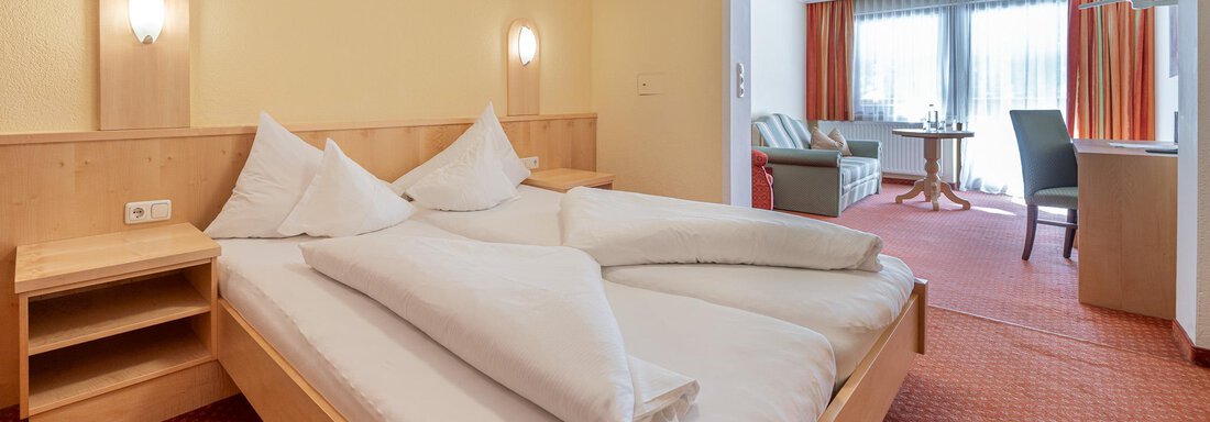 Ein gemütliches Hotelzimmer mit einem großen Doppelbett und zwei Kissen. Das Zimmer hat warmes Licht und einen schönen Blick auf den Aufenthaltsbereich. - Hotel Schöpf - Gries