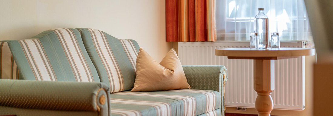 Ein helles Zimmer mit einem gestreiften Sofa und einem kleinen Tisch. Auf dem Tisch stehen Wasserflasche und Gläser. - Hotel Schöpf - Gries