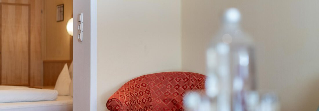 Ein gemütlicher Raum mit einem roten Sessel und einem Tisch. Im Hintergrund ist ein Bett und ein Bild an der Wand sichtbar. - Hotel Schöpf - Gries