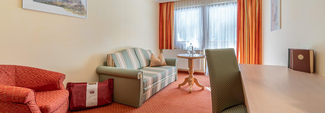 Ein helles Zimmer mit einem gemütlichen Sofa und einem Stuhl. Der Raum hat große Fenster mit Vorhängen und eine warme Farbgestaltung. - Hotel Schöpf - Gries