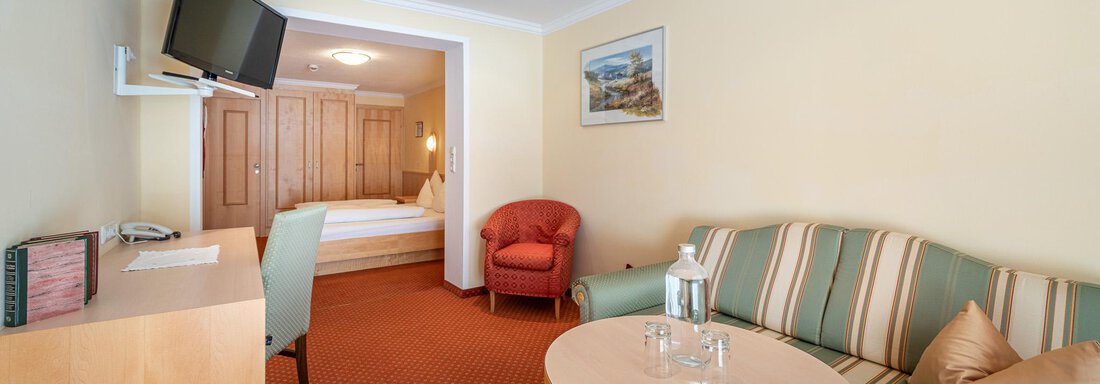 Ein gemütlicher Hotelzimmer mit einem Sofa, einem Tisch und einem Fernseher. Im Hintergrund ist ein bequemes Bett und ein Schrank sichtbar. - Hotel Schöpf - Gries
