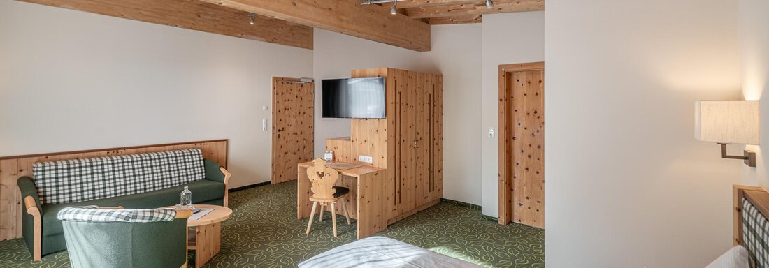 Zimmer (Zirbensuite Plus 315) 2 Ein einladendes Zimmer mit Holzbalkendecke und gemütlicher Einrichtung. Es gibt ein Doppelbett, einen Wohnbereich und einen Fernseher. - Hotel Schöpf - Gries