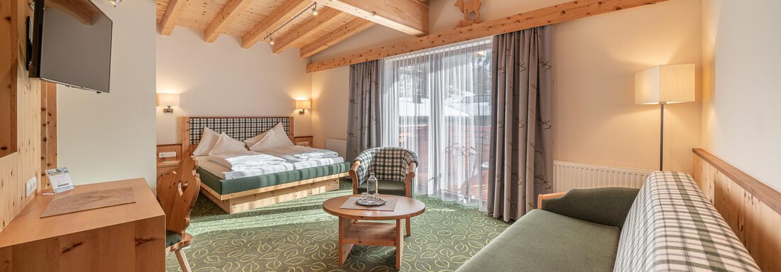 Ein gemütliches Zimmer mit Holzverkleidung und hohen Decken. Es gibt ein Doppelbett, eine Sitzecke und große Fenster, die Tageslicht hineinlassen. - Hotel Schöpf - Gries