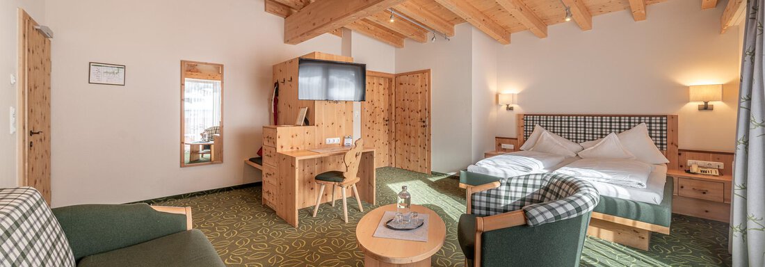 Ein gemütliches Zimmer mit Holzdecke, einem großen Bett und einem Sitzbereich. Die Einrichtung ist modern und freundlich, mit einem grünen Teppich und einem Fernseher. - Hotel Schöpf - Gries