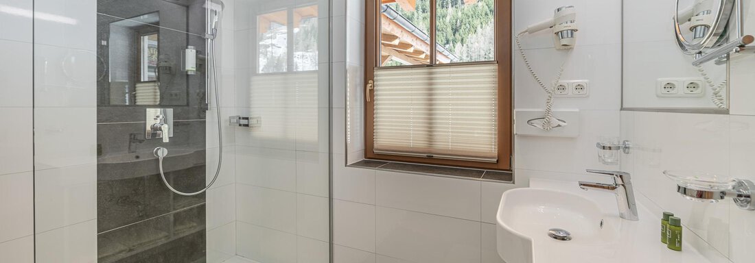 Ein modernes Badezimmer mit einer begehbaren Dusche und einem Waschbecken. Ein Fenster sorgt für natürliches Licht und eine angenehme Atmosphäre. - Hotel Schöpf - Gries