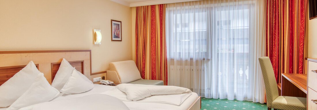 DZ 1 Ein helles Hotelzimmer mit einem großen Bett und flauschigen Kissen. Der Raum ist freundlich eingerichtet und hat große Fenster mit Vorhängen. - Hotel Schöpf - Gries