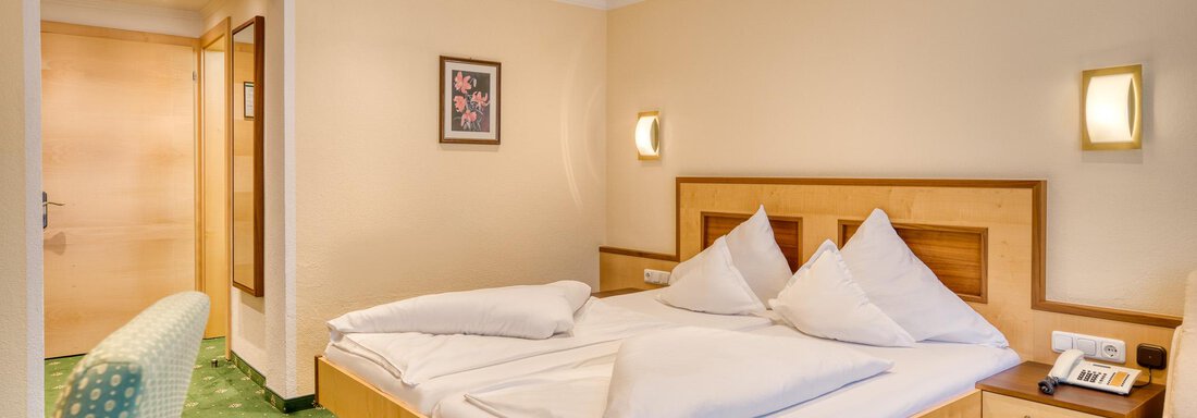 Ein gemütliches Hotelzimmer mit einem Doppelbett und zwei Kissen. An den Wänden sind moderne Lampen und ein Bild dekoriert. - Hotel Schöpf - Gries