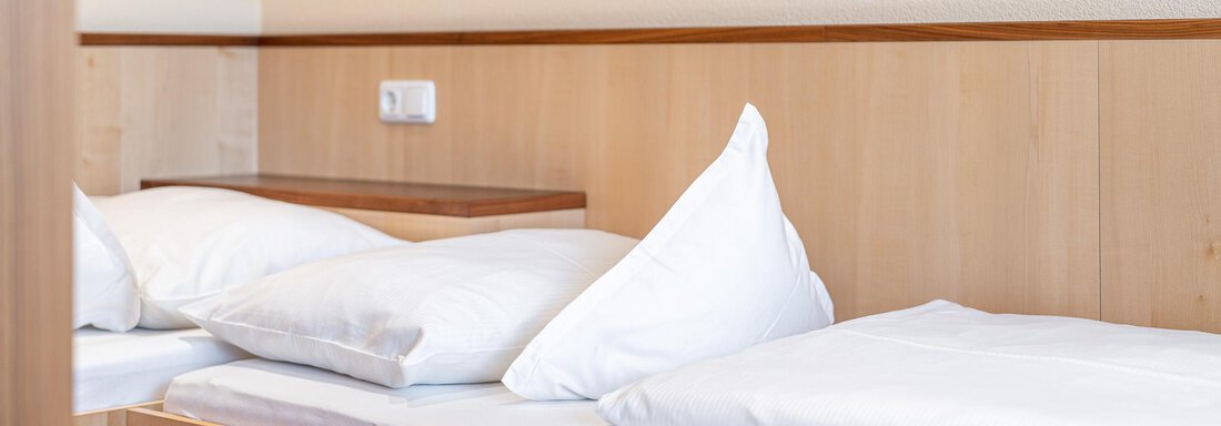 Ein einfaches Bett mit weißen Kissen und Decken in einem modernen Raum. Die Wände sind aus hellem Holz, was eine gemütliche Atmosphäre schafft. - Hotel Schöpf - Gries