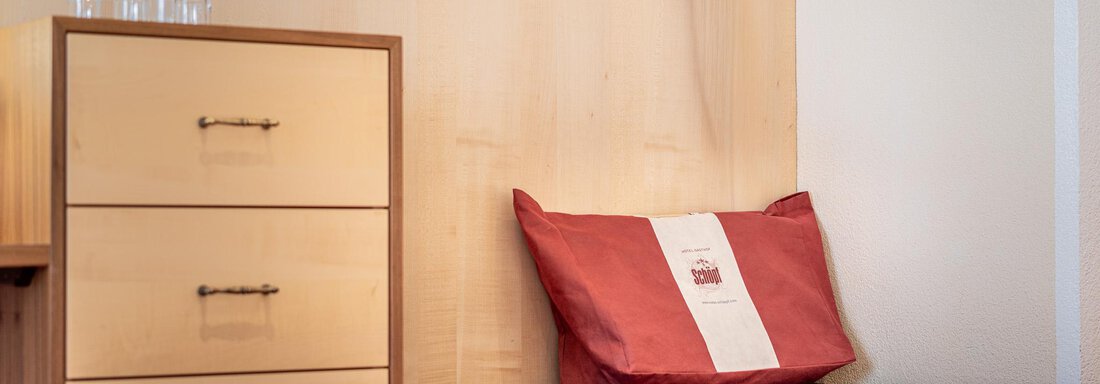 Ein schlichtes Zimmer mit einem Holzschrank und einem roten Kissen. Im Hintergrund stehen Gläser auf dem Tisch. - Hotel Schöpf - Gries
