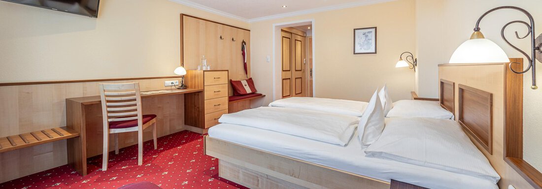 Ein gut ausgestattetes Hotelzimmer mit zwei Betten und einem roten Teppich. Der Raum verfügt über einen Schreibtisch und einen Fernseher an der Wand. - Hotel Schöpf - Gries