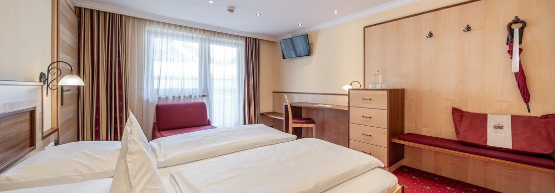 Ein großes Zimmer mit zwei Einzelbetten und einem gemütlichen Sitzbereich. Das Licht ist hell und die Fenstervorhänge sind geöffnet, was eine einladende Atmosphäre schafft. - Hotel Schöpf - Gries
