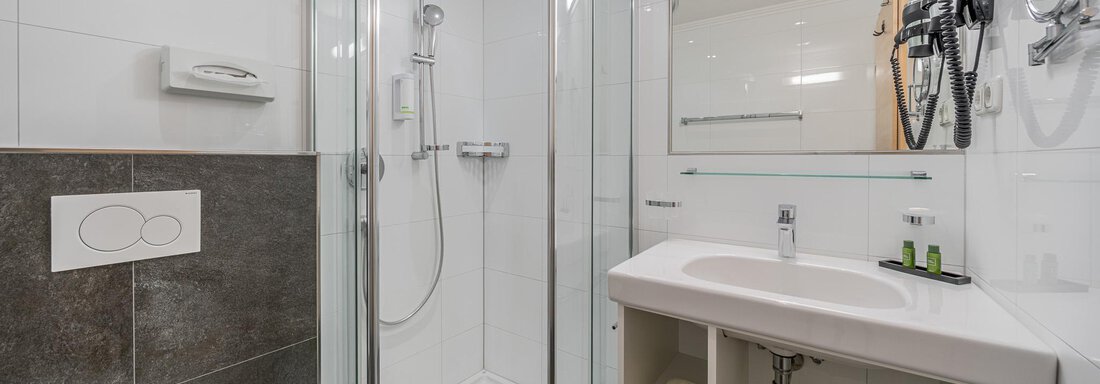 Ein modernes Badezimmer mit einer gläsernen Dusche und einem Waschbecken. Die Wände sind hell gefliest und spiegelt eine saubere, entspannende Atmosphäre wider. - Hotel Schöpf - Gries