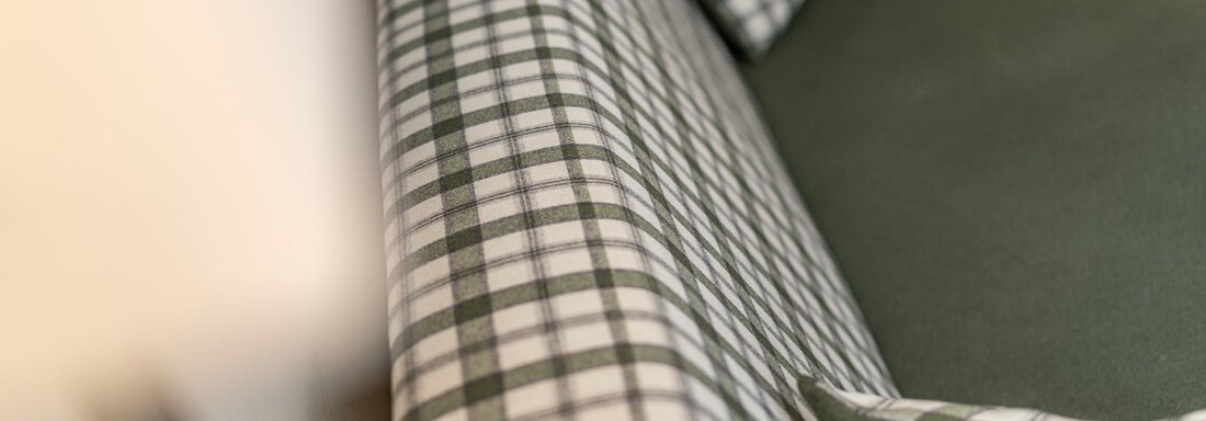 Ein gemütliches Sofa mit einem karierten grünen Bezug und einem dazu passenden Kissen. Die Polsterung vermittelt ein einladendes Ambiente. - Hotel Schöpf - Gries