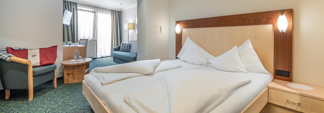 Ein modernes Hotelzimmer mit einem Doppelbett und einem gemütlichen Sitzbereich. Große Fenster sorgen für eine helle und einladende Atmosphäre. - Hotel Schöpf - Gries