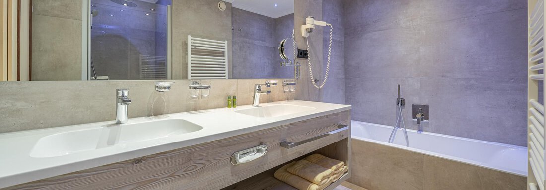 Ein modernes Badezimmer mit einer eleganten Badewanne und einem Waschtisch. Die Wände sind in neutralen Farben gehalten, und es gibt eine angenehme Beleuchtung. - Hotel Schöpf - Gries