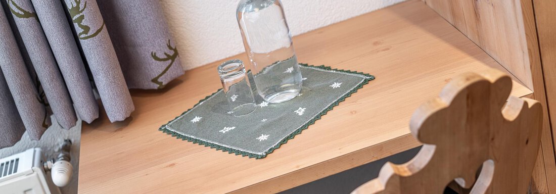 Ein Tisch aus hellholz mit einer Flasche Wasser und einem Glas. Daneben liegt eine grüne Platzdecke. - Hotel Schöpf - Gries