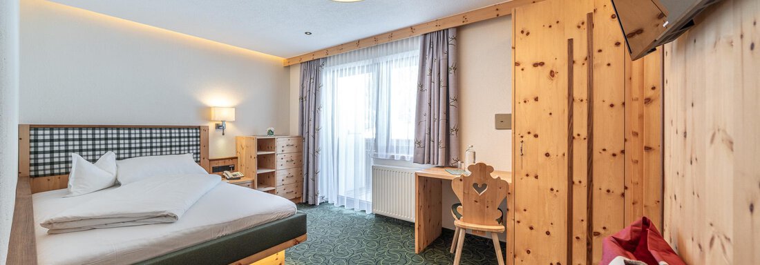Ein modernes Hotelzimmer mit einem komfortablen Doppelbett und Holzinterieur. Im Raum befindet sich ein Schreibtisch und ein Fenster mit Blick nach draußen. - Hotel Schöpf - Gries