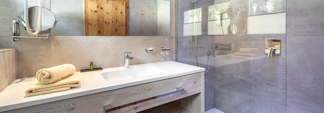 Ein modernes Badezimmer mit einer gläsernen Dusche und einem hellen Waschbecken. Holz- und graue Elemente sorgen für eine elegante Atmosphäre. - Hotel Schöpf - Gries
