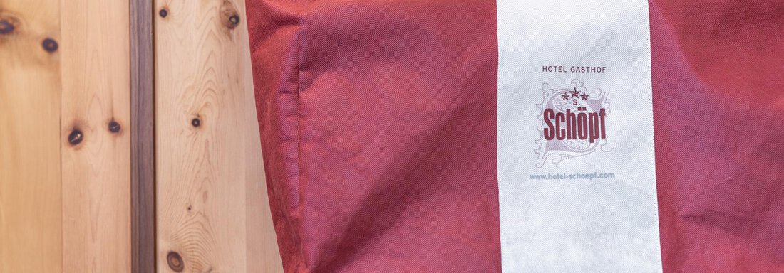 Ein rotes Paket mit einem weißen Etikett, das das Hotel Schöpt markiert. Im Hintergrund ist eine Holzwand und ein grünes Tuch sichtbar. - Hotel Schöpf - Gries
