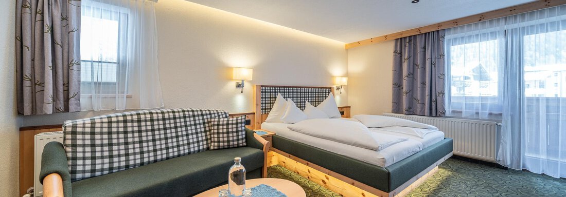 Zimmer (Zirbensuite 203) 11 Ein gemütliches Hotelzimmer mit einem Doppelbett und einer Sitzecke. Es gibt große Fenster, die viel natürliches Licht hereinlassen. - Hotel Schöpf - Gries