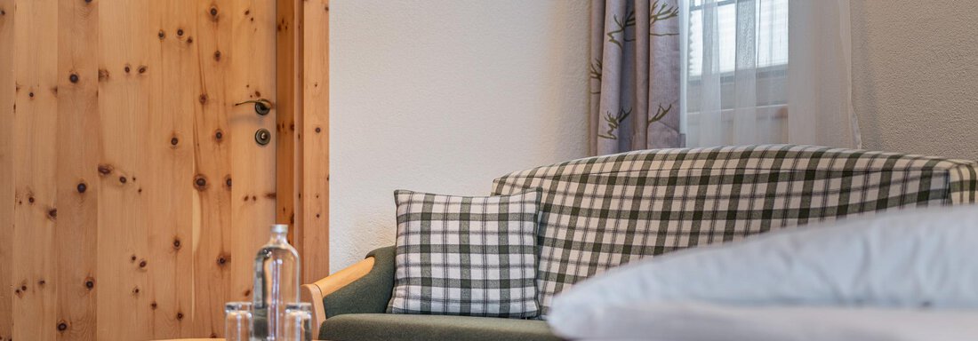 Ein gemütlicher Raum mit einem Sofa und einem kleinen Holztisch. Im Hintergrund sieht man eine Holztür und ein Fenster mit Vorhängen. - Hotel Schöpf - Gries