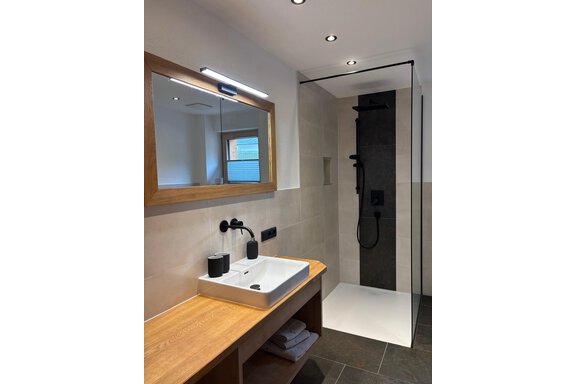 Bad_WC A modern bathroom with an elegant shower and a wooden vanity. The walls are bright tiled and the lighting creates a pleasant ambiance. - KLAMMERHOF - Gries