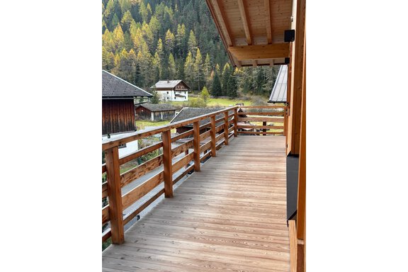 A spacious wooden terrace with a beautiful view of the surrounding mountains and forests. Some houses can be seen in the background, surrounded by autumn trees. - KLAMMERHOF - Gries
