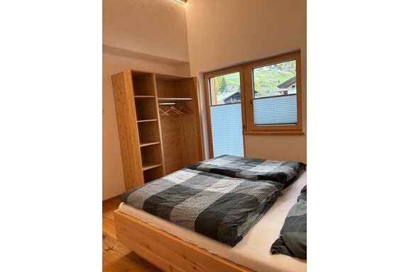 A cozy bedroom with two beds and a wooden wardrobe. Through the window, one looks out at a green landscape. - KLAMMERHOF - Gries