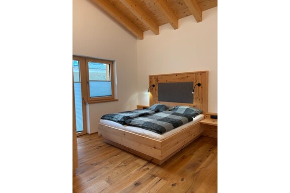 A modern bedroom with a wooden bed and inviting, checkered bedcovers. Large windows let in plenty of daylight and create a friendly atmosphere. - KLAMMERHOF - Gries