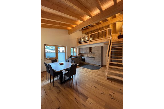 A modern kitchen with a dining table and chairs. The room has bright wooden ceilings and friendly windows for plenty of daylight. - KLAMMERHOF - Gries