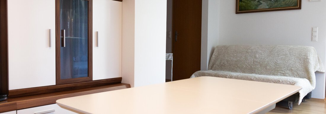Ein helles Wohnzimmer mit einem Esszimmertisch und einem Sofa. An der Wand hängt ein Landschaftsgemälde und es gibt einen modernen Schrank. - Ferienhaus Neurauter - Haiming