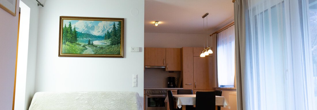 Ein gemütlicher Wohnraum mit einem Sofa und einem Gemälde an der Wand. Im Hintergrund sieht man eine moderne Küche mit einem Essbereich. - Ferienhaus Neurauter - Haiming