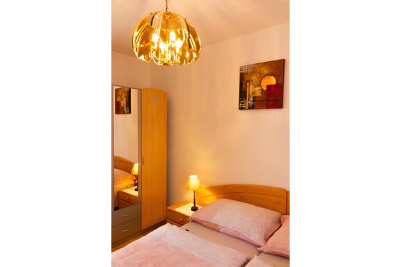 Ein gemütliches Schlafzimmer mit einem Holzbett und weichen Kissen. Ein großer Spiegel und eine ansprechende Lampe sorgen für eine angenehme Atmosphäre. - Ferienhaus Neurauter - Haiming