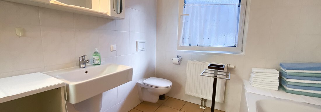 Ein modernes Badezimmer mit einem Waschbecken, einer Toilette und einer Badewanne. Das Zimmer hat helle Fliesen und ein Fenster, das natürliches Licht hereinlässt. - Ferienhaus Neurauter - Haiming