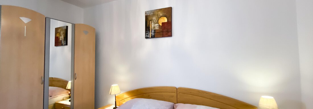 Ein gemütliches Schlafzimmer mit einem Doppelbett und sanften Farben. Zwei Nachttische mit Lampen und ein Kleiderschrank ergänzen die Einrichtung. - Ferienhaus Neurauter - Haiming