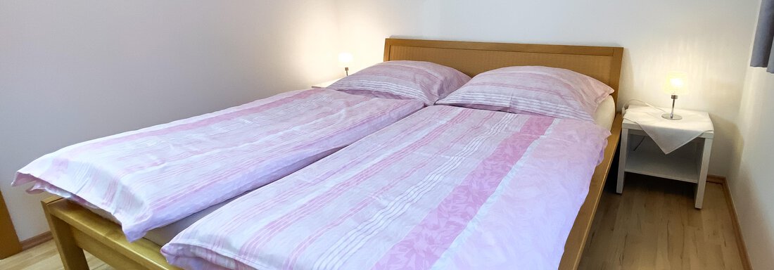 Ein gemütliches Schlafzimmer mit einem Doppelbett und rosa Bettwäsche. Die Wände sind hell und die Beleuchtung sorgt für eine angenehme Atmosphäre. - Ferienhaus Neurauter - Haiming