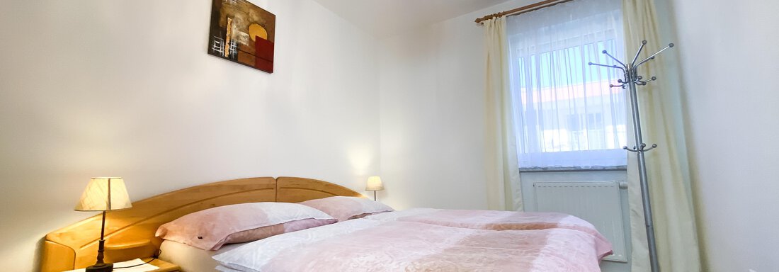 Ein gemütliches Schlafzimmer mit einem Doppelbett und einem warmen Farbton. Das Zimmer hat ein Fenster mit Vorhängen und eine schöne Deckenlampe. - Ferienhaus Neurauter - Haiming