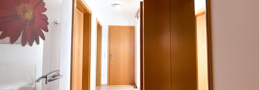 Ein heller Flur mit Holzfußboden und weißer Wandfarbe. An der Wand ist eine große Blume abgebildet, und es gibt mehrere Türen. - Ferienhaus Neurauter - Haiming